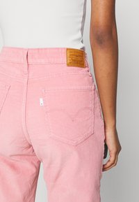 Różowe spodnie w sztruks z tylnymi kieszeniami zdobionymi subtelnym, sercowym przeszyciem oraz brązową skórzaną metką marki na pasku.