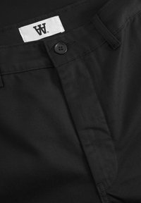 Black fabric pants featuring a smooth texture, a button closure, and a white label with black lettering near the waistline.