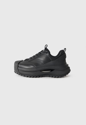 Schwarze Sneakers mit einer klobigen Silhouette, strukturiertem Obermaterial, durchbrochenen Mustern, Schnürverschluss und dicker Gummisohle mit Profil.