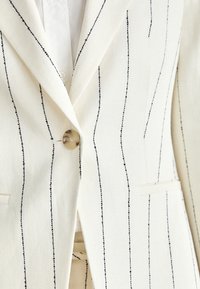Witte op maat gemaakte blazer met zwarte verticale strepen, voorzien van een notch-revers, één knoopsluiting en gestructureerde zakken.