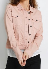 Rosa denimjacka med två bröstfickor, svarta knappar och en kortad passform. Tyget verkar mjukt med en subtil textur.