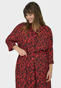 Rood en zwart luipaardprint jurk, lange mouwen, knoopsluiting aan de voorkant, ceintuur in de taille, vloeiende ontwerp met een zachte, gestructureerde stof.