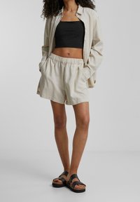 Shorts en lin beige avec une taille élastique et des poches latérales, associés à un crop top noir et des sandales à lanières noires.
