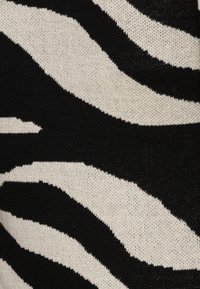 Kangas musta-valkoinen, jossa on seepra-raita kuvio, ja teksturoitu neule. Raidat vaihtelevat leveydessä ja muodossa materiaalin yli.