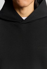 Felpa nera con cappuccio dalla texture morbida, caratterizzata da una tasca frontale e un logo discreto in filo scuro nell'angolo inferiore sinistro.