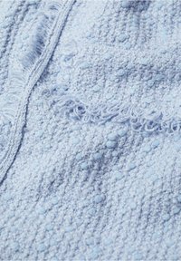 Gros plan de tissu texturé bleu clair avec de petites bosses en relief et des bords tissés effilochés.