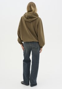 Rövidített olívazöld kapucnis pulóver, laza szabású sötétkék farmernadrággal párosítva. Simas texture és egyszerű dizájn, nincsenek látható minták.