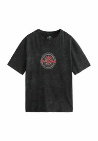 Zwarte, losse t-shirt met een ronde grafiek met "DE VERRADERS" in vet rood. Gemaakt van textuurstof met een vervaagd uiterlijk.