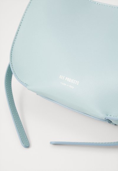 Sac bandoulière en cuir bleu clair avec une finition lisse, doté d'une sangle fine et d'un texte en relief "REE PROJECTS fabriqué en Italie."