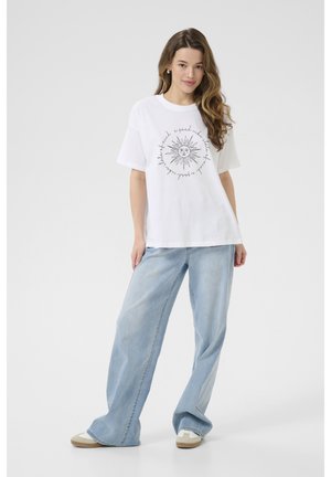 Vit bomullströja med en solgrafik med strålar och svart text, ihop med ljusblå vida denimjeans.