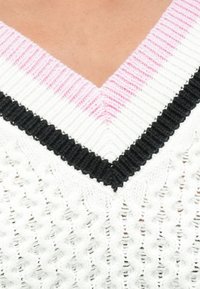 Strik v-hals sweater med hvid bund, der har lyserøde og sorte stribede detaljer på den ribbede krave og et struktureret mønster over hele.