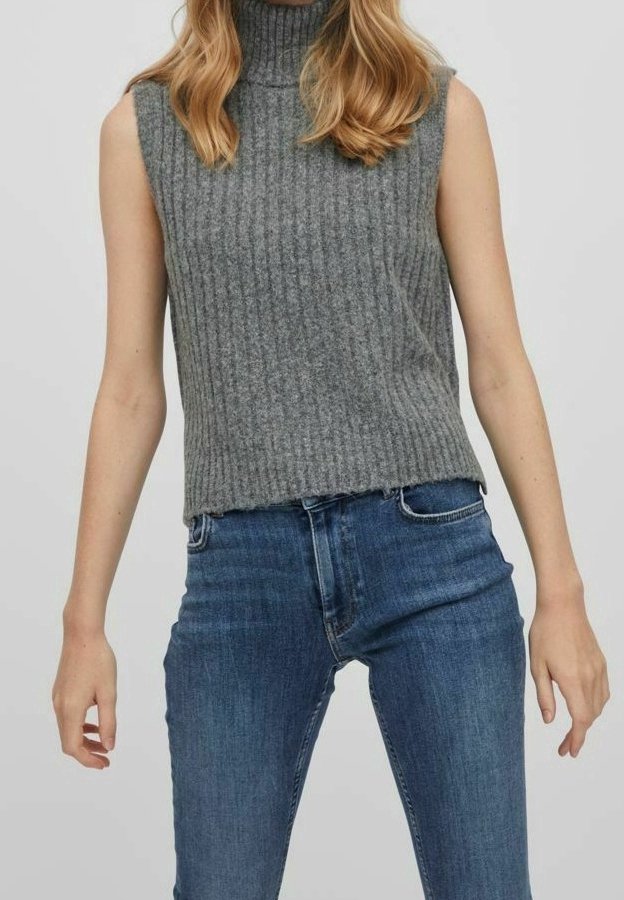 Pull à col roulé sans manches en tricot côtelé gris porté avec un jean taille haute bleu sur une personne debout.