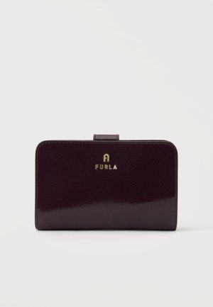 Tamsiai violetinė Furla piniginė su maža sklende ir auksiniu logotipu priekyje per vidurį, pateikta ant balto fono.