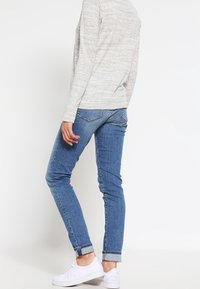 Jasnoszara bluzka z długim rękawem zestawiona ze średnio niebieskimi dopasowanymi dżinsami, z podwiniętymi mankietami i białymi trampkami. Prosty, codzienny strój.