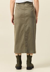 Olivenfarbener Midirock aus Baumwolle, mit geradem Schnitt, Gesäßtasche und Nahtdetail, kombiniert mit schwarzen und grünen Ankle Boots.