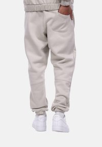 Light gray sweatpants with elastic cuffs and a back pocket, paired with white sneakers featuring a logo on the heel.