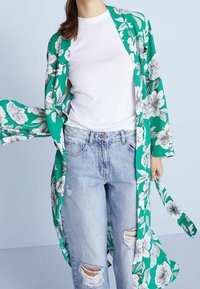 Grøn blomsterkimono med hvide blomster mønstre, parret med en hvid T-shirt og slidte blå jeans. Letvægtigt stof og flydende design.