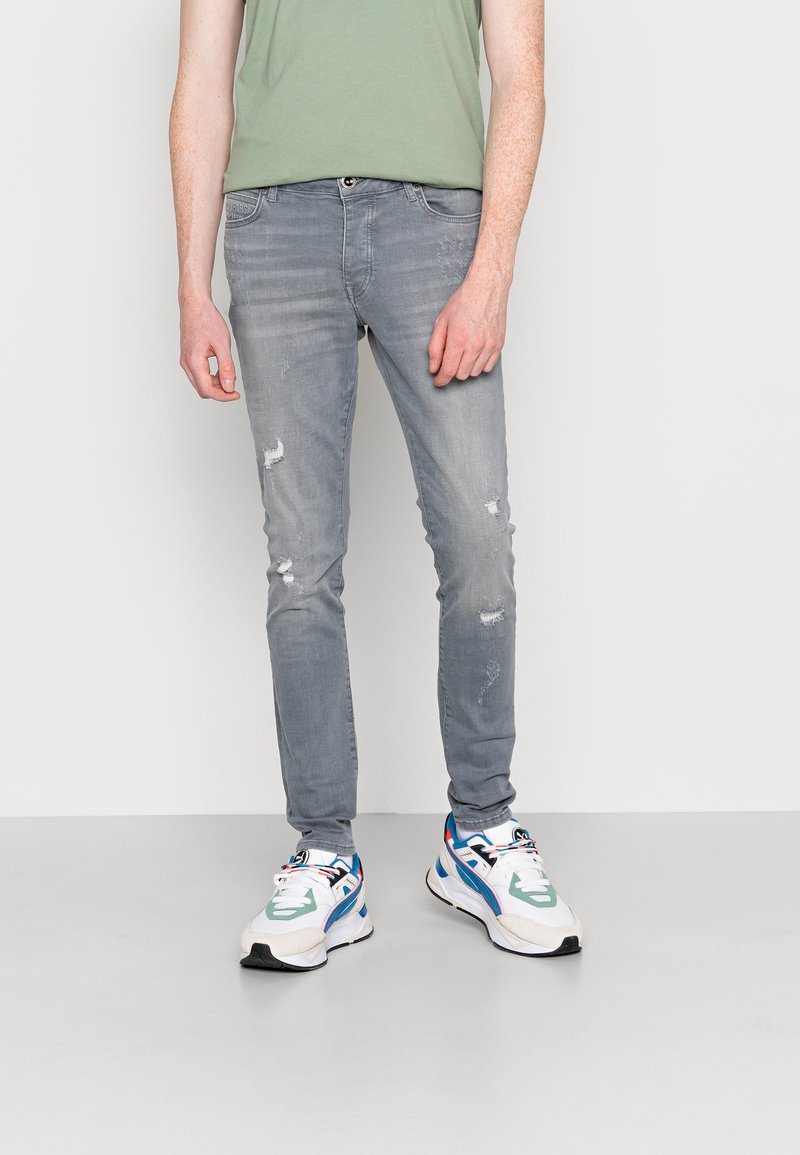 Lichtgrijze skinny jeans met versleten details, gedragen met multikleurige sneakers met blauwe, groene en witte accenten.