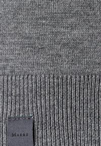 Grauer gestrickter Stoff mit einer glatten Textur und einem gerippten Saum. Verfügt über ein angenähtes Stoffetikett in der unteren linken Ecke.