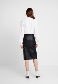 Vit långärmad blus i kombination med en svart läderpenkjol och vita ankelstövlar. Outfiten har en slät textur och skräddarsydd passform.