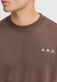 Brun sweatshirt med ribbet krave, med hvid "A.R.C." branding på venstre side, lavet af blødt stof med en glat tekstur.