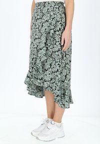 Jupe midi florale avec un fond noir et des motifs floraux verts, ourlet volanté et coupe décontractée, associée à des baskets blanches.