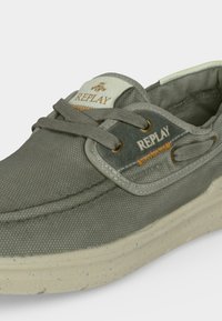 Καθημερινό γκρι υφασμάτινο παπούτσι με κορδόνια και μπεζ σόλα με στίγματα, με τη μάρκα "REPLAY" στη γλώσσα και στο πλευρικό πάνελ με ορειχάλκινα κορδόνια.