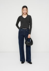 Svart ribbet topp med lange ermer og nagledekor i halsen, kombinert med løse blå denimjeans og en liten svart skinnhåndveske.