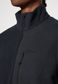 Schwarze Fleece-Zip-Jacke mit hohem Kragen, ausgestattet mit einer Vorderentasche mit Reißverschluss und einem gestickten Logo auf der Brust.