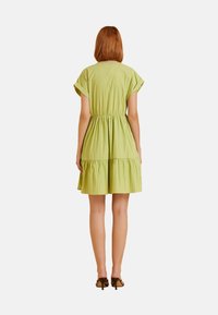 Abito in cotone verde con maniche corte, corpino aderente, vita elastica e gonna a strati. Tessuto morbido, lunghezza sopra il ginocchio, dettagli arricciati.