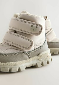 Beige og grå vandtætte støvler med to velcroremme, tekstureret overdel og et panda ansigt detalje på siden. Kraftig gummisål.