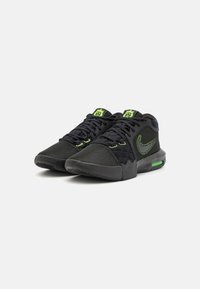 Scarpe sportive nere con parte superiore in rete, dettagli verdi e un'unità air visibile nella suola. Presentano motivi testurizzati e chiusura con lacci.