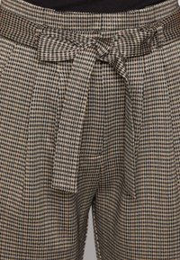 Hnědé a krémové kostkované kalhoty s látkovým páskem a záhybovým předním dílem. Materiál má strukturovanou vazbu a přiléhavý střih.