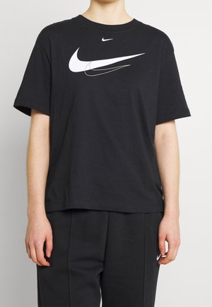 Person iført en sort Nike t-shirt med tre hvide swoosh-logoer og matchende sorte bukser med et lille Nike swoosh på venstre lår.
