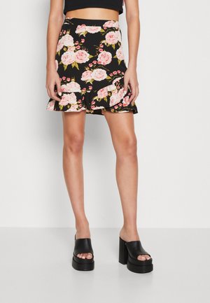 Fekete virágmintás szoknya rózsaszín rózsákkal, réteges fodros szegéllyel és feszes derékrésszel. Csinos fekete platform szandálokkal párosítva.