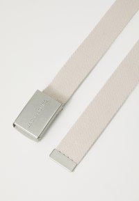Beige vævet stofbælte med en sølv metalspænde graveret med "JACK & JONES," der har rene kanter og en jævn overflade.