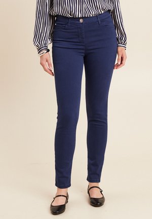 Jeans skinny bleu marine avec une texture lisse, dotés d'une fermeture à bouton à l'avant et de poches latérales discrètes, associés à un chemisier rayé.