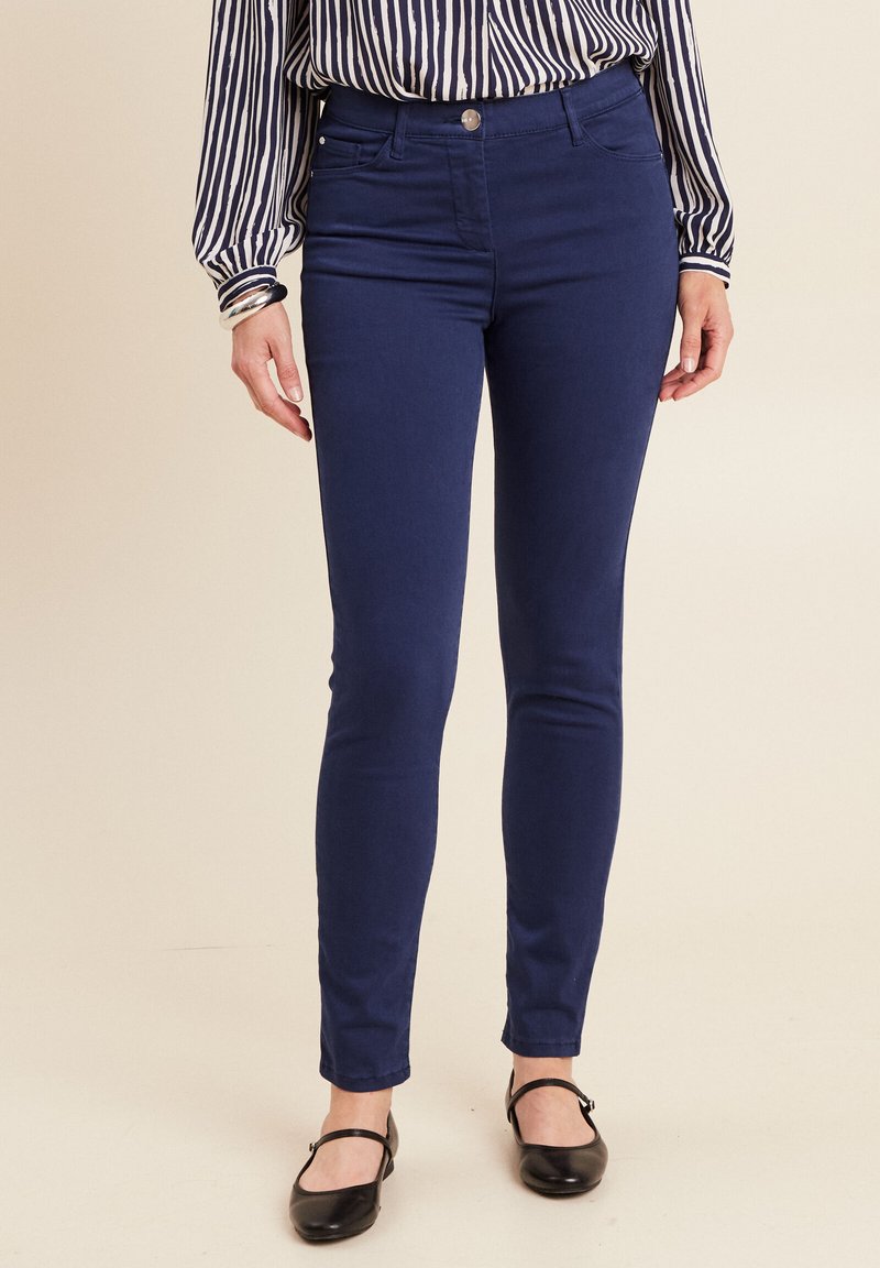 Marineblauwe skinny jeans met een gladde textuur, voorzien van een knoopsluiting aan de voorkant en subtiele zijzakken, gecombineerd met een gestreept blouse.