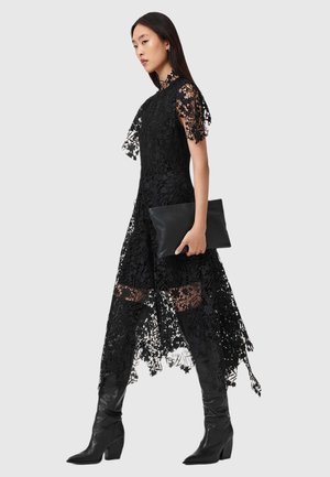 Rochie din dantelă neagră cu model floral, mâneci scurte, decolteu înalt, panouri transparente și fustă asimetrică. Combinate cu cizme negre până la genunchi și un clutch.