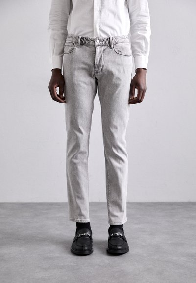 Lichtgrijze denim jeans met een slim fit, vijf zakken en subtiele vervaging. Gecombineerd met zwarte instappers en een wit overhemd met lange mouwen.