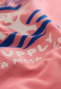 Rosa Stoff mit blauem und weißem grafischem Design und teilweise sichtbarem Text, einschließlich "UPPLAY" und "MESA".