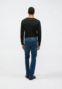 Musta pitkähihaine paita ja siniset farkut, joita käyttää henkilö, näkymä takaa. Farkuissa on suora lahje ja minimaalinen yksityiskohta.