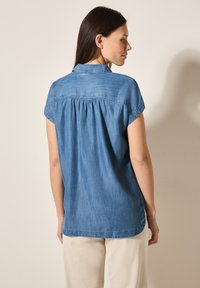 Denim overhemd met korte opgerolde mouwen, detail van een plooien aan de achterkant en een gebogen zoom. Blauw stoffen textuur, casual pasvorm, ontworpen voor comfort.