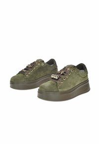 Un paio di sneakers platform in suede verde oliva con lacci scuri e decorazioni di stelle metalliche e gioielli sul davanti.