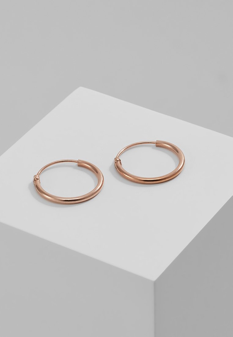Brincos em forma de argola em ouro rosa com um design suave e arredondado. O metal brilhante tem um acabamento polido e uma aparência leve.