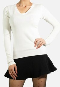 Haut à manches longues blanc avec un décolleté en V, fabriqué en tissu tricoté doux. Associé à une jupe noire évasée et des collants à pois.