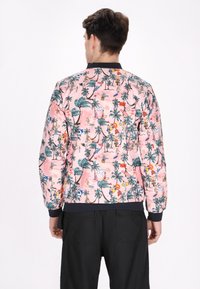 Roze bomberjack met een tropische print van palmboomontwerpen, zonmotieven en zomeractiviteiten. Geribbelde marineblauwe kraag en manchetten.