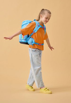 Blauer Rucksack mit rosa Akzenten und Blumenmustern; orangefarbenes T-Shirt; hellblaue Jeans; gelbe Schuhe; stehend mit ausgestreckten Armen.