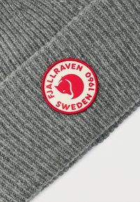 Harmaa neulottu pipo, jossa on ribbineulepinta. Siinä on pyöreä punainen ja kerma logo, jossa lukee "FJÄLLRÄVEN SWEDEN 1960".