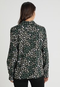 Camisa de manga larga con fondo negro que presenta patrones de estrellas multicolores en blanco, verde y beige; textura de tela suave.